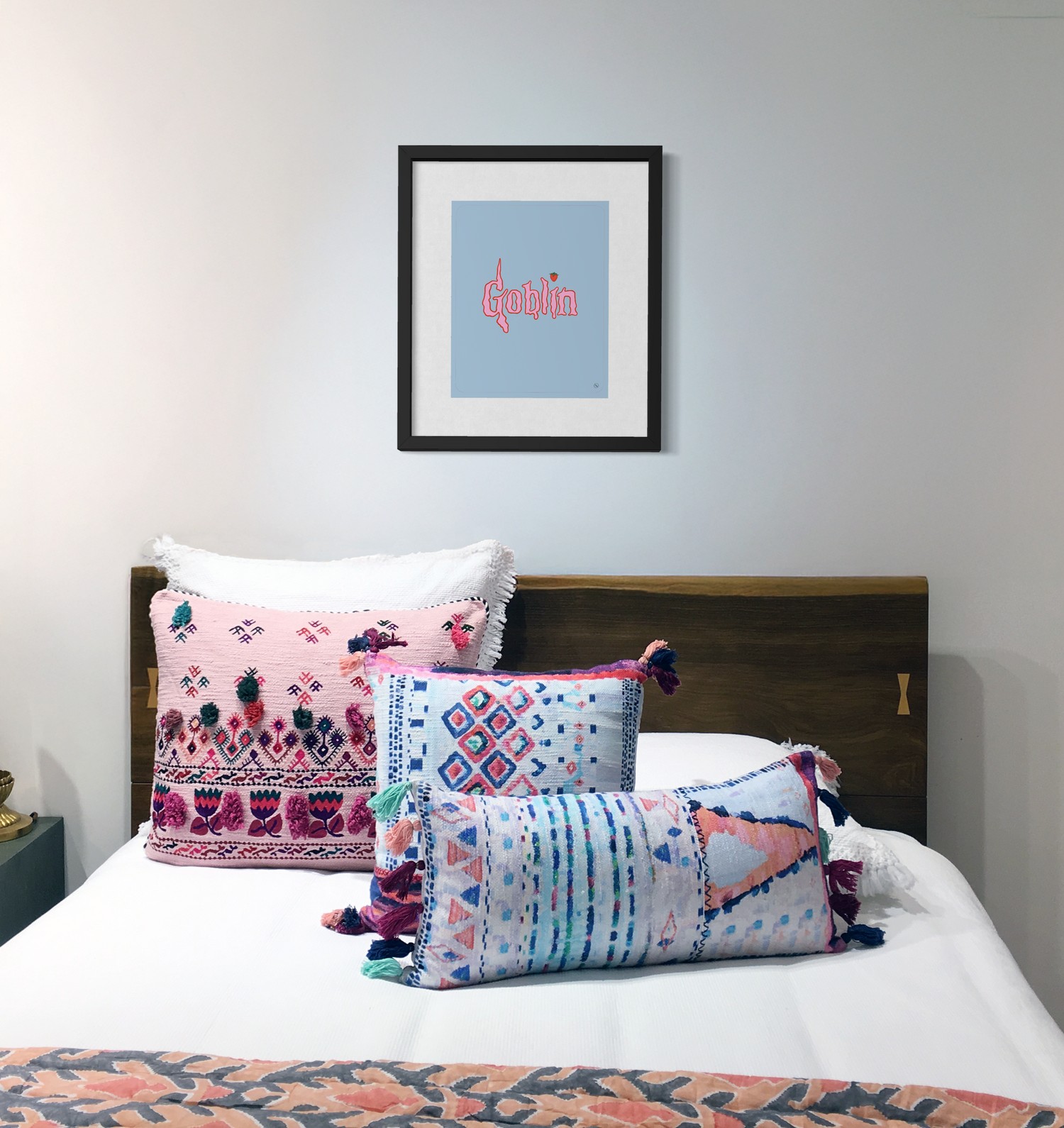 Decorative pillows on a bed with a framed drawing that says "Goblin" on the wall.